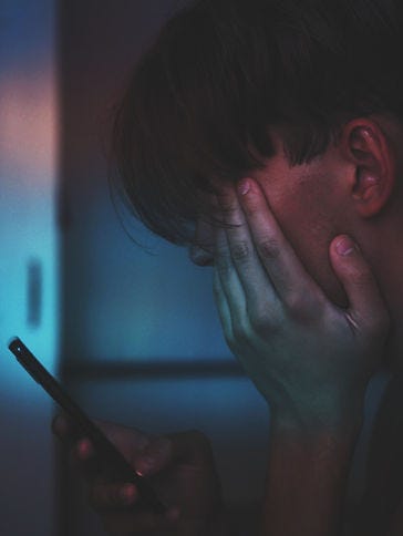 Photo of a woman, who seems upset, with her hand on her face looking down at her phone.