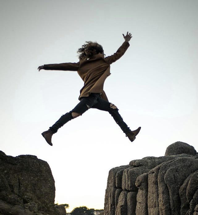 person jumping on big rock under gray and white sky during daytime person jumping on big rock under gray and white sky during daytime