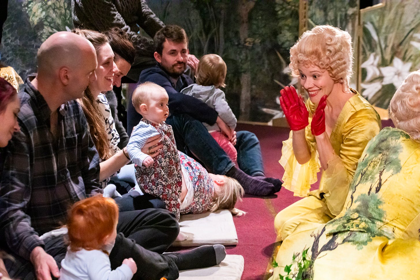 An opera singer in a yellow dress performs for parents and babies at the ENO