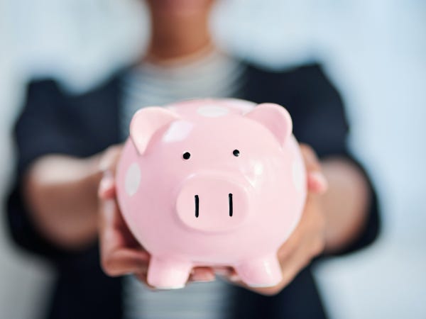 Dark skinned woman holding a piggy bank to the camera