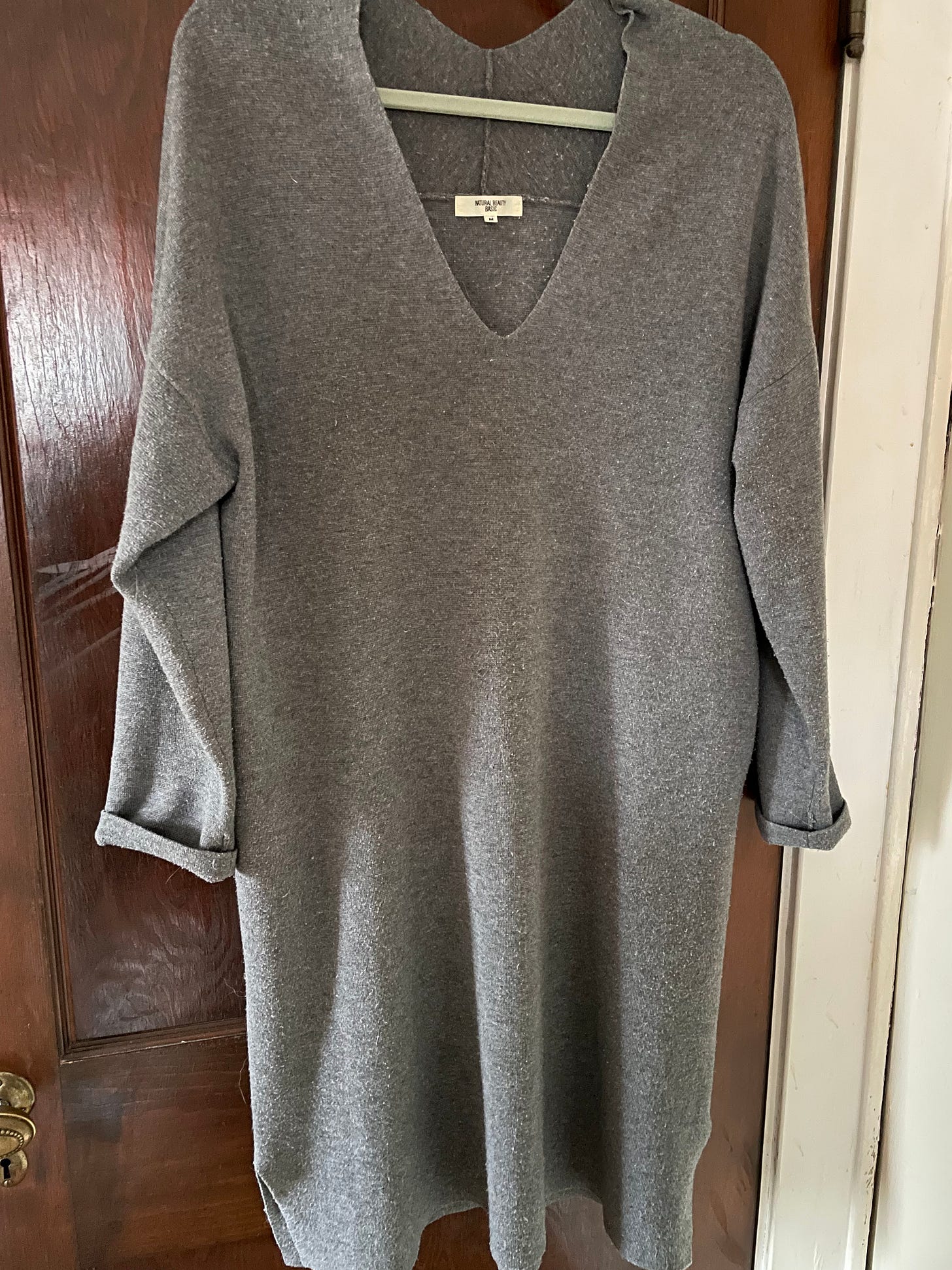 A gray knit dress with a v-shaped neckline hanging on a hook on a dark brown wood door