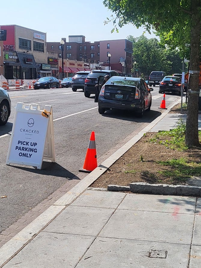 Image shows Connecticut Avenue facing south from the sidewalk with a cracked eggery sign for pickup and orange cones. Traffic is passing through and a car is parked in the spot.
