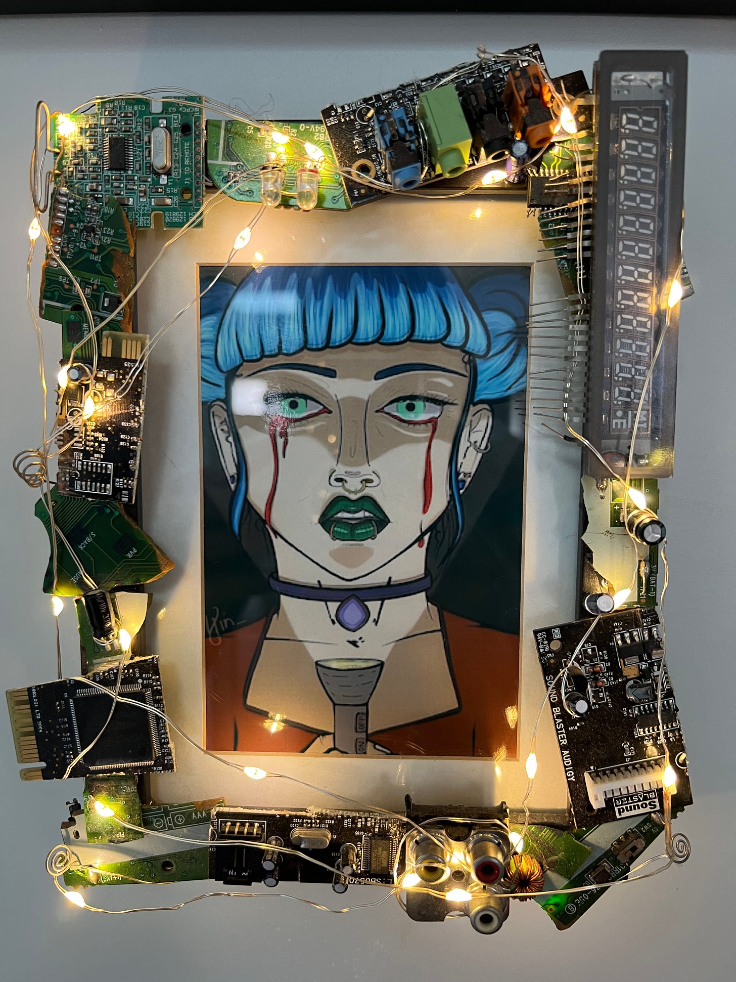a framed digitally drawn portrait of a girl with blue hair. Blood is dripping from her eyes. She holds a flashlight up to her face. She has green lipstick, a nose ring, and two lip rings.