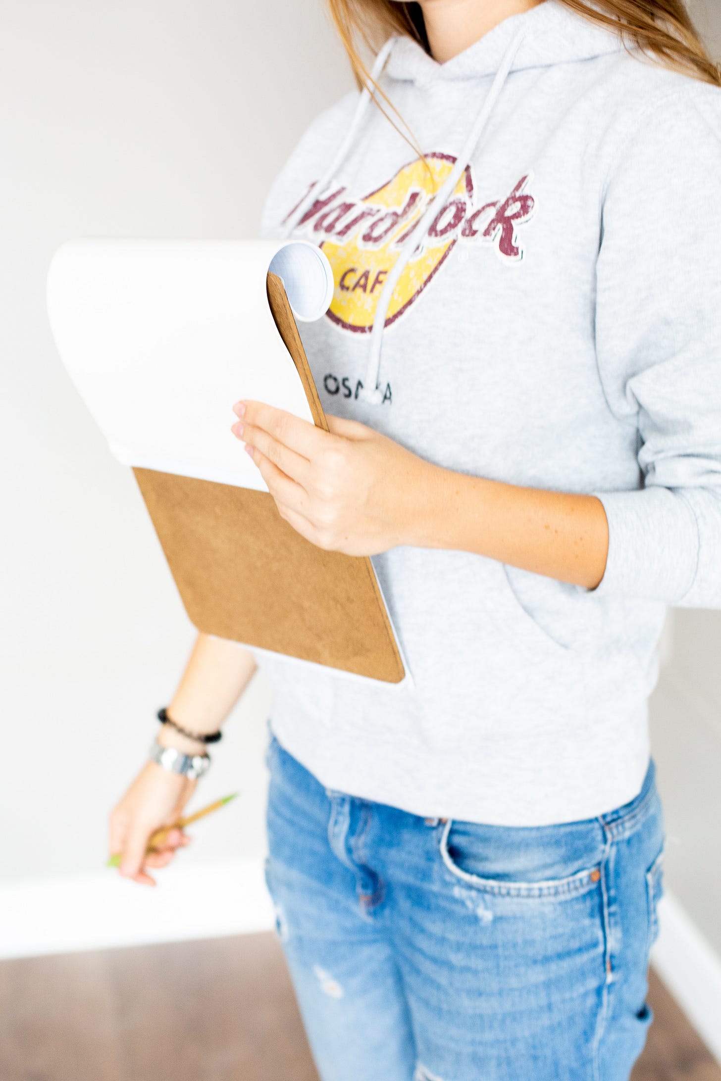 woman wearing a grey hoodie and jeans carrying a clipboard.