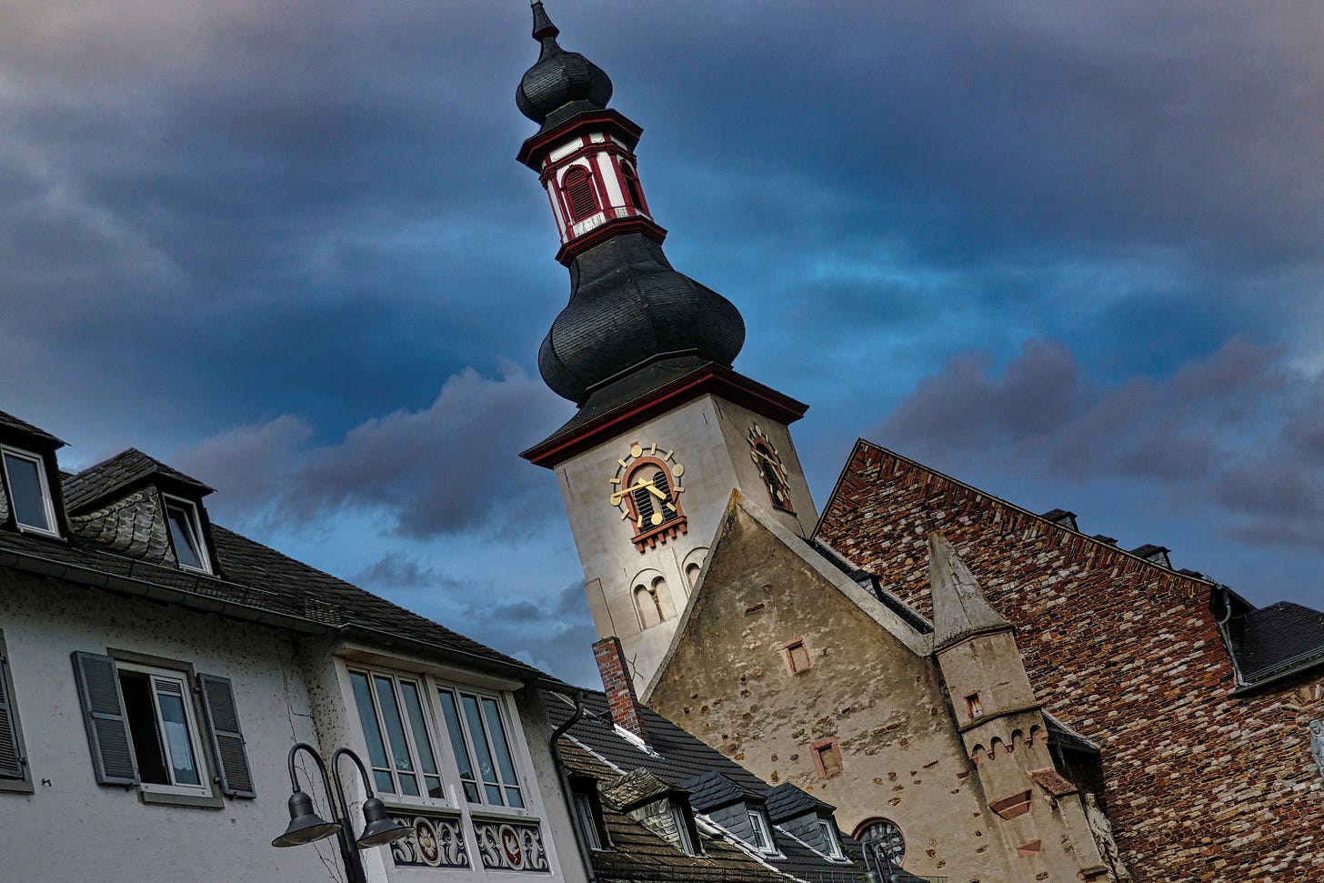 Buildings and a clock steeple tilted in the composition with dark blue and grey clouds in the sky