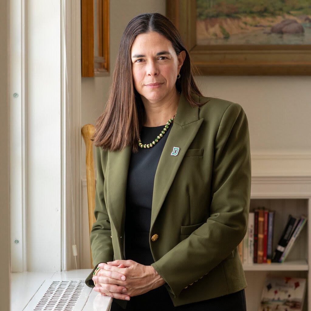 A portrait of Sian Beilock, the president of Dartmouth College, standing by a window in an olive-green blazer. 