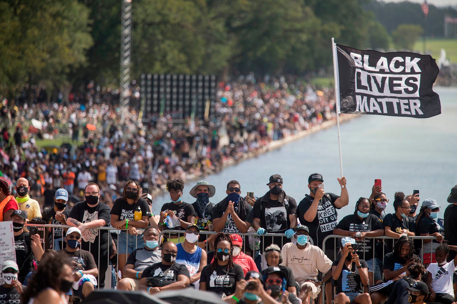 Thousands stand behind a barricade, most wearing facemasks, as US residents flood the streets of Washington DC in the 2020 March for Our Lives, in support of the Black Lives Matter Movement