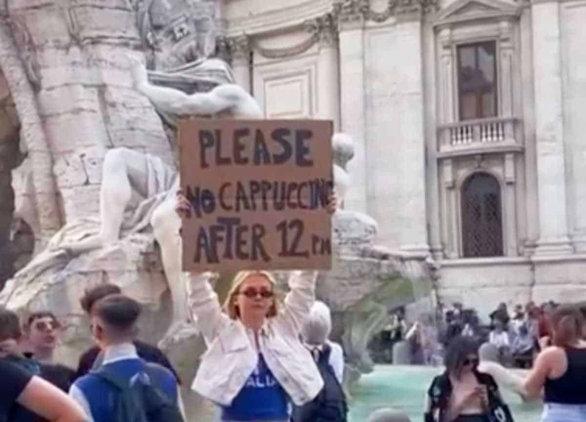 Immagine dal video della ragazza di fronte alla Fontana di Trevi che alza il cartello per i turisti “Per favore, non ordinate un cappuccino dopo mezzogiorno”