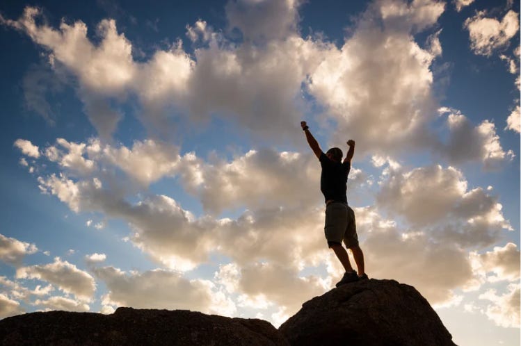 A man stands on a rock with his hands overhead in triumph.