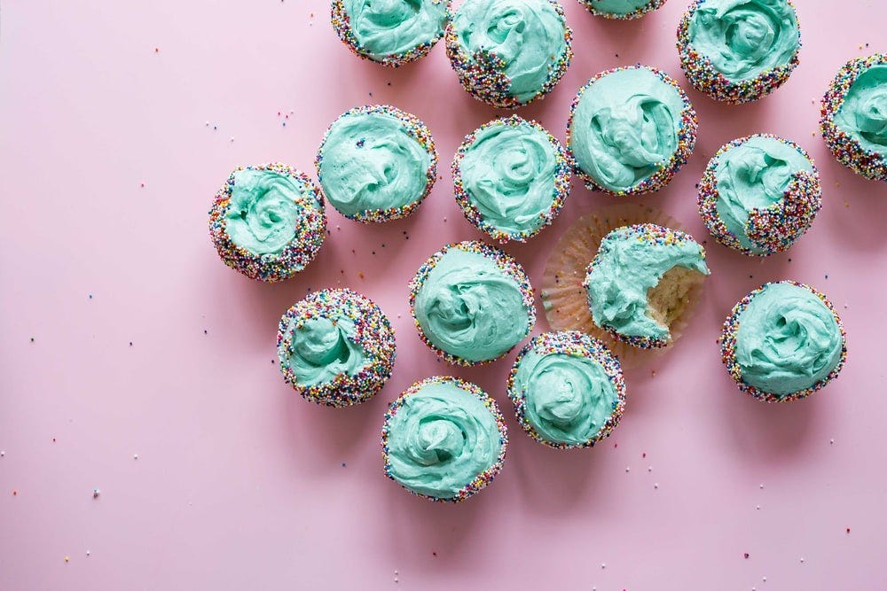 Cupcakes with teal icing and sprinkles on a pink table