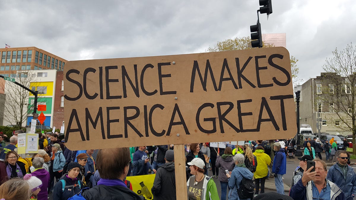 A person holds a cardboard sign that reads “Science Makes America Great” during a protest. A person holds a cardboard sign that reads “Science Makes America Great” during a protest.