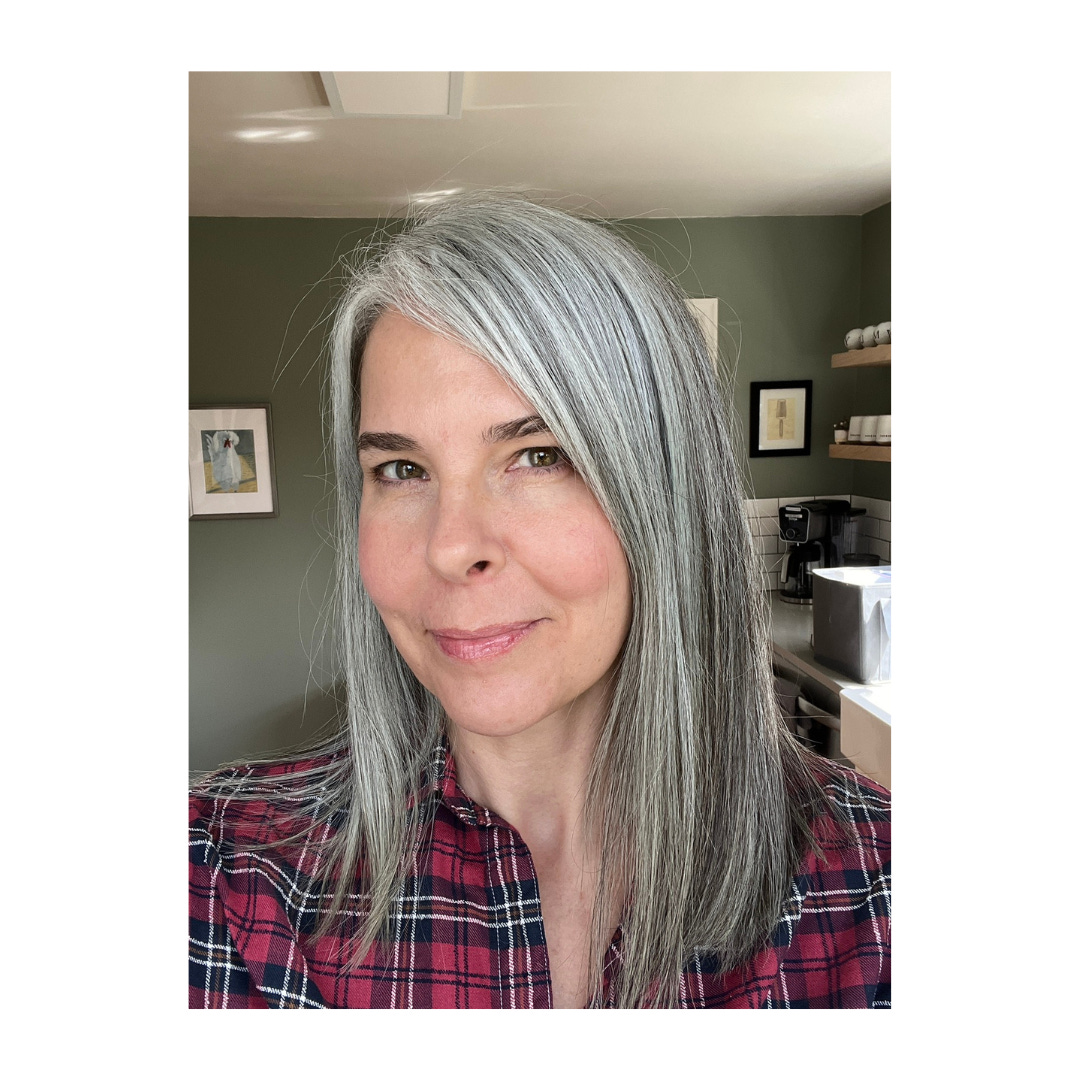 A selfie of Whitney, a white woman in her mid-40s with shoulder-length gray hair. She is smiling and her head tilts slightly to the side.