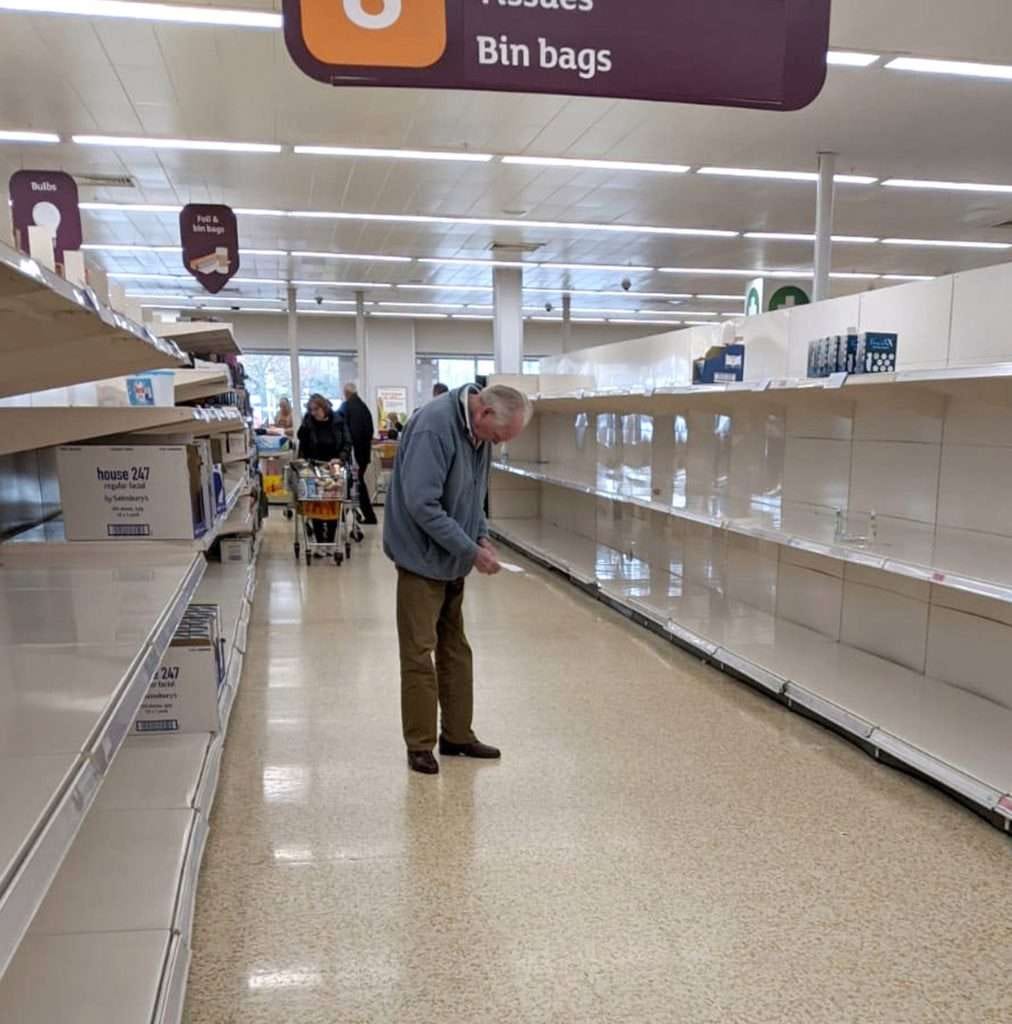 Photo of a shopper staring at his grocery list in a store with bare shelves