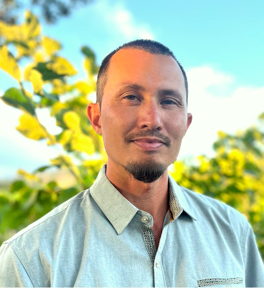 Gino head shot standing in front of trees and a light blue sky