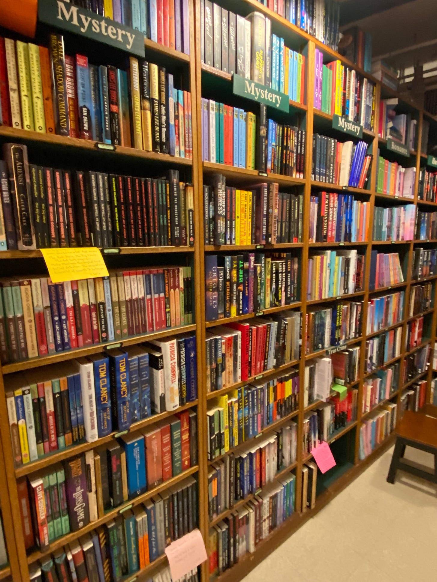 A row of mystery novels on tall shelves in a bookstore, with signs labeling them "Mystery" at the top.