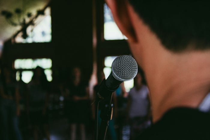 A man standing in front of a microphone (in focus), about to speak to a crowd.