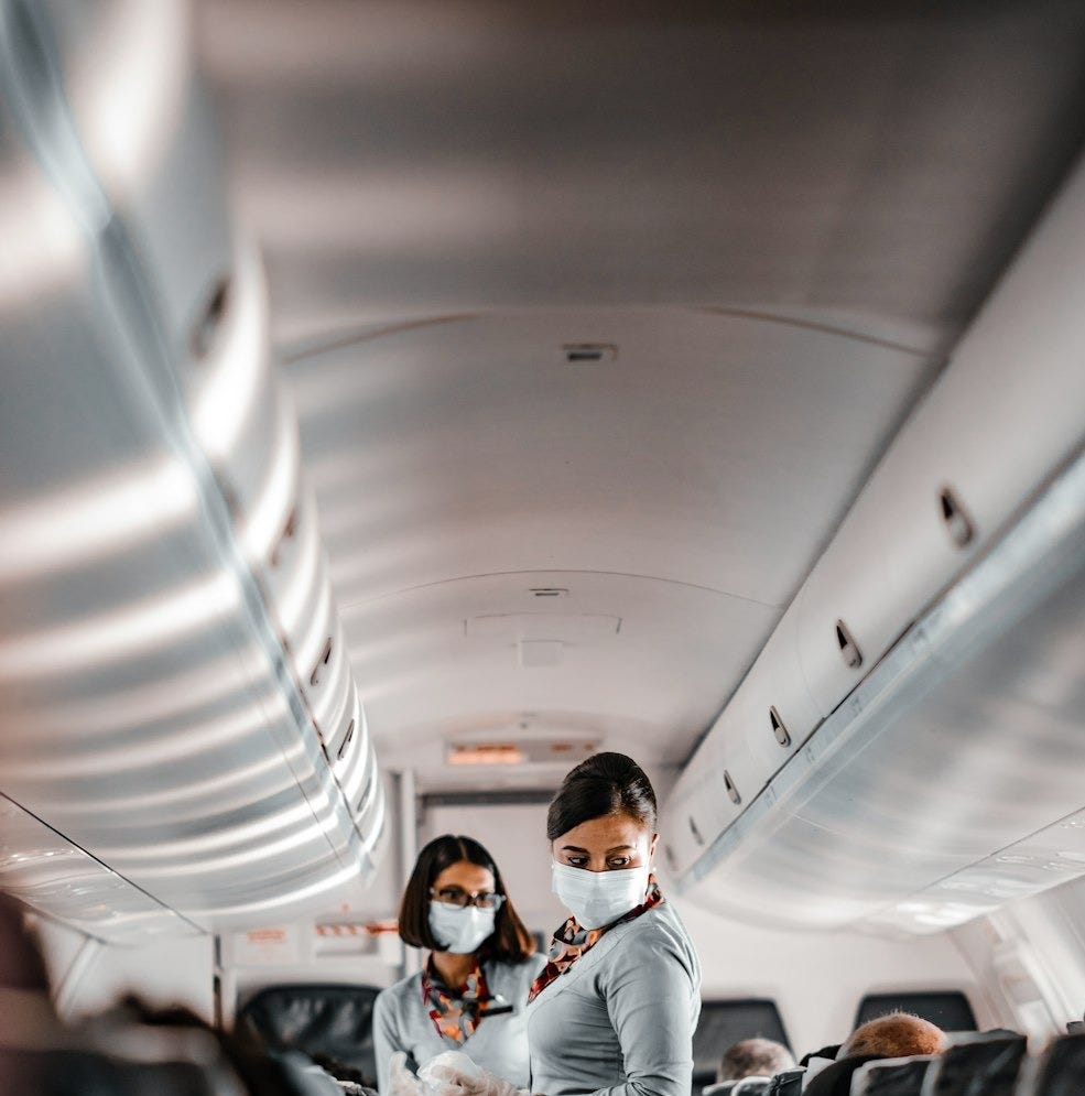 air hostess wearing a facemask standing in the aisle of an aeroplane