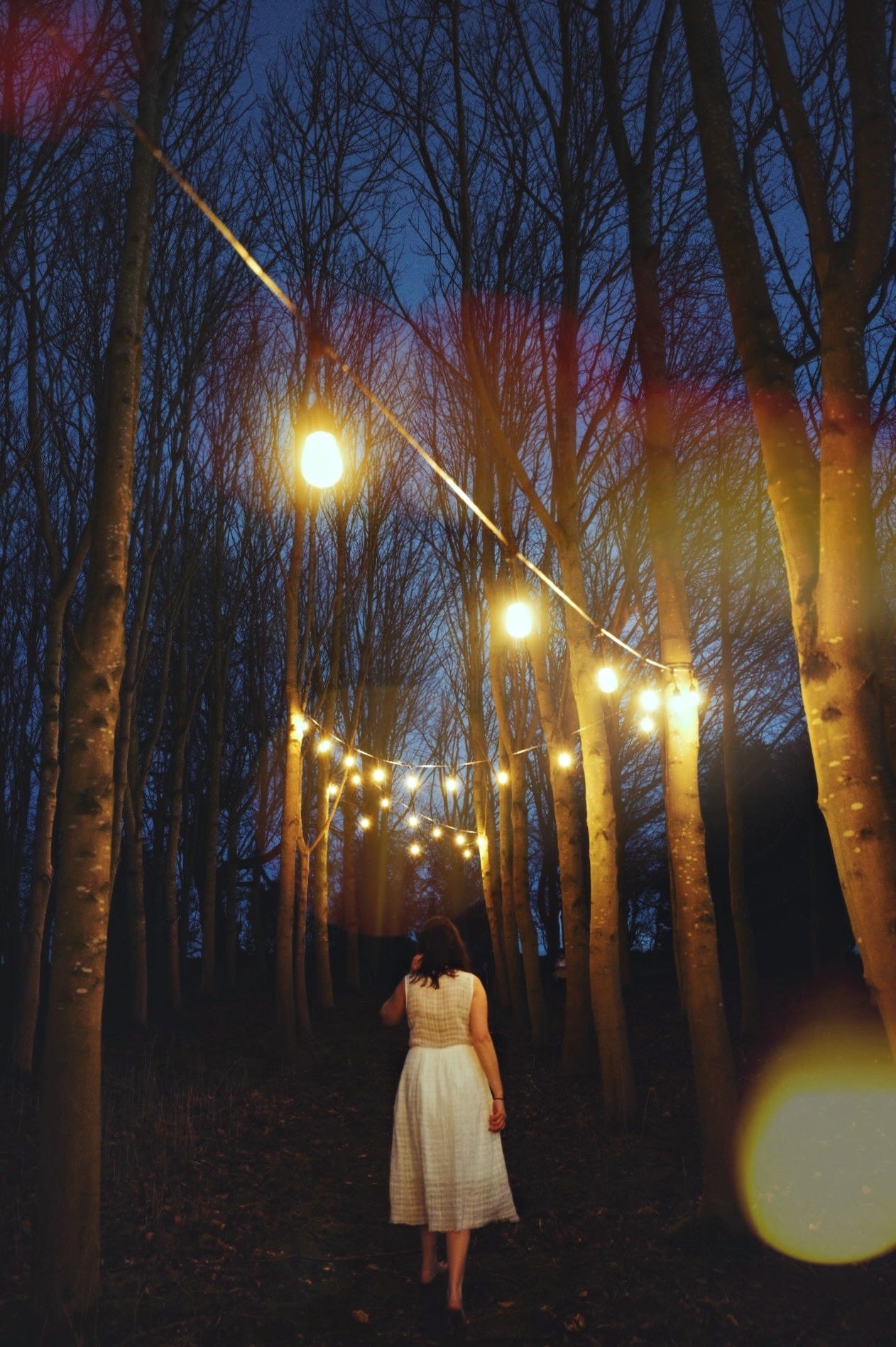 me, walking barefoot through a forest at night. Yellow lights are strung overhead to light my path.
