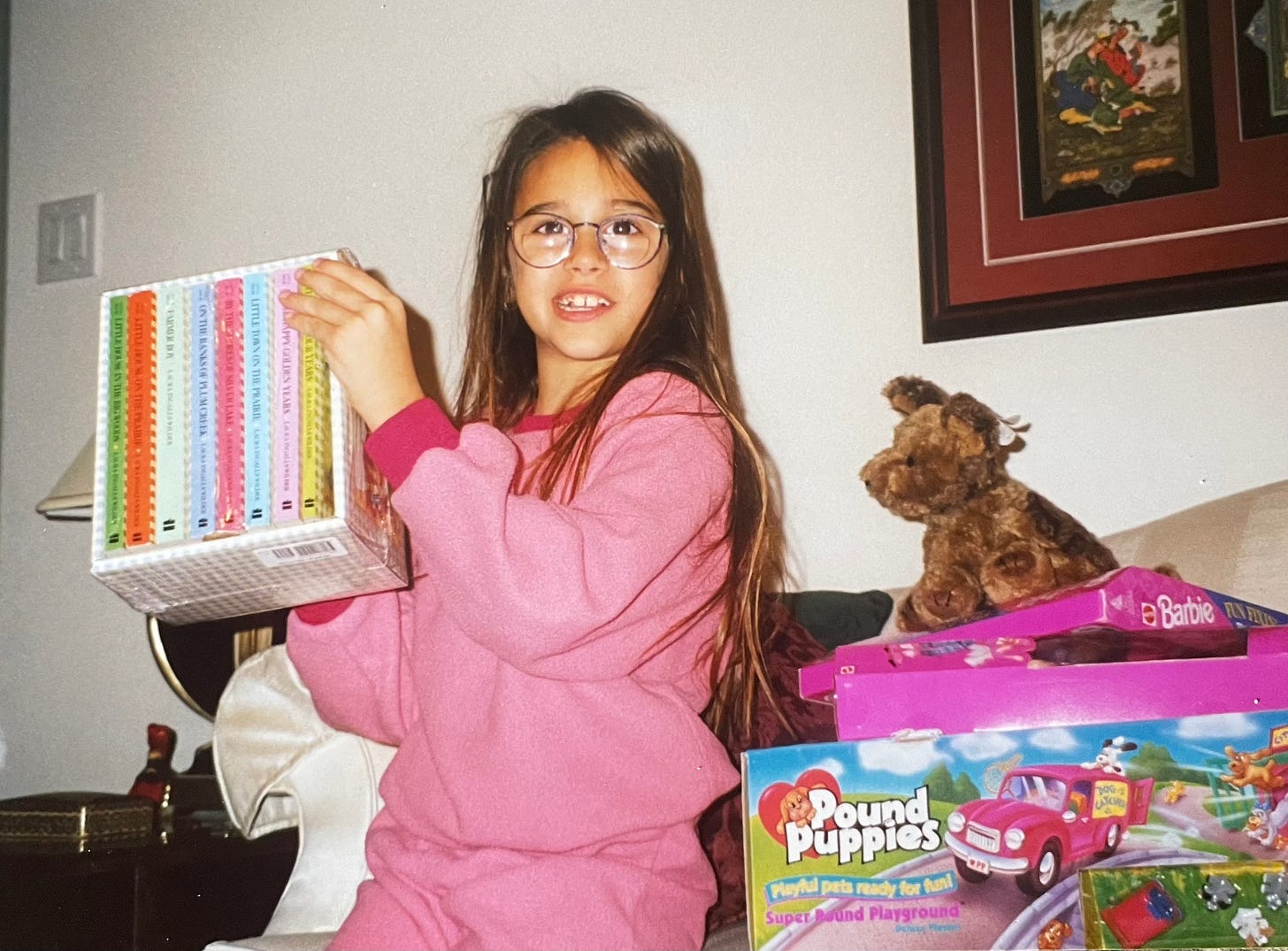 An old photo of a young Shohreh in big glasses holding up a box set of BoxCar Children books she got on Christmas morning