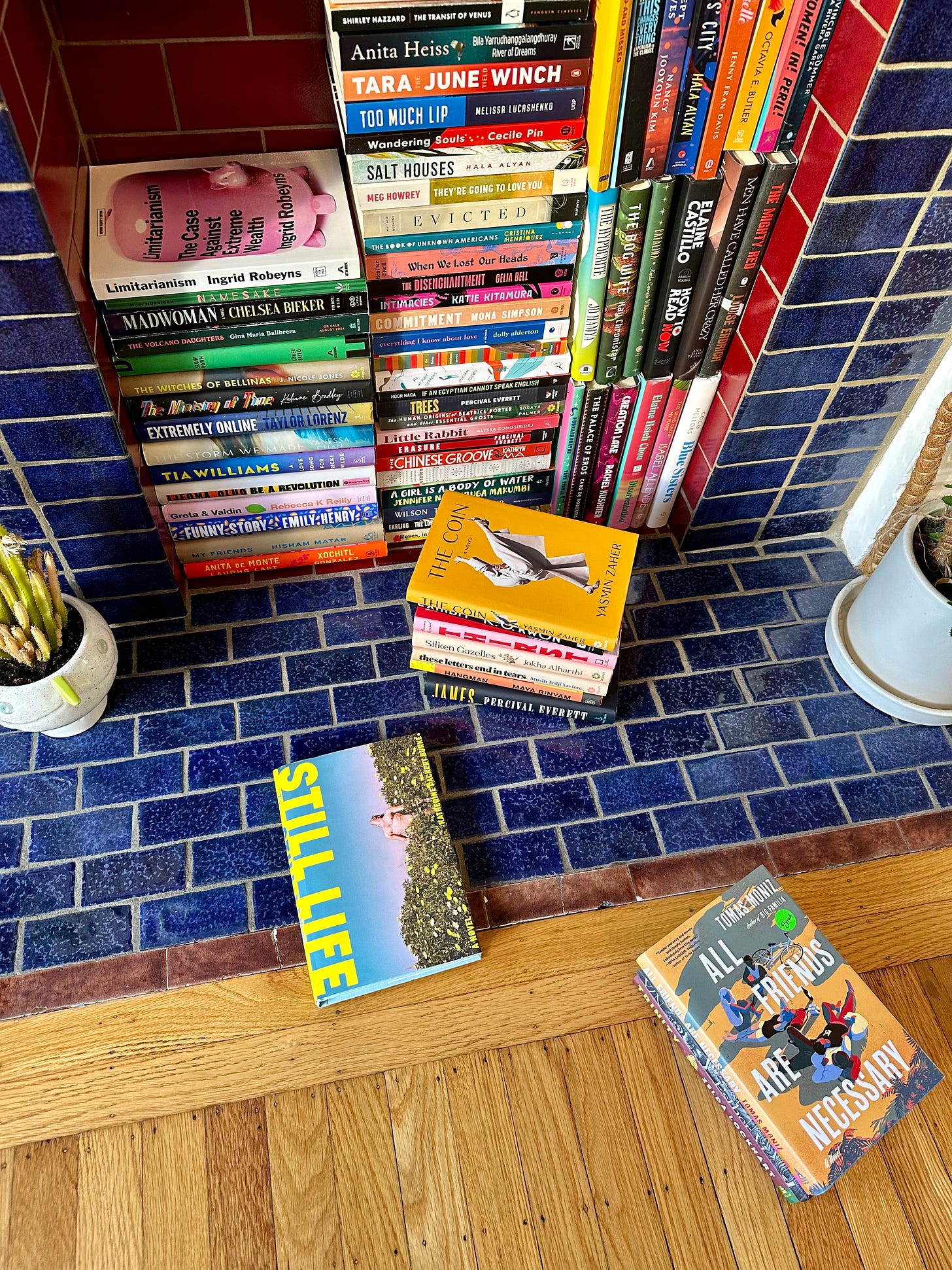 A blue tiled fireplace full of books. Still Life rests on the ground apart from the rest.