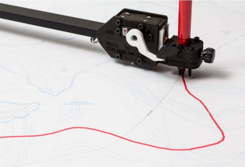 Close up of a robotic arm that is drawing an irregularly curved red line on white paper that already has faint cartographic lines on it. The Moving Borders project which hosted this installation show borders along a glacier between Austria Italy do indeed shift.  