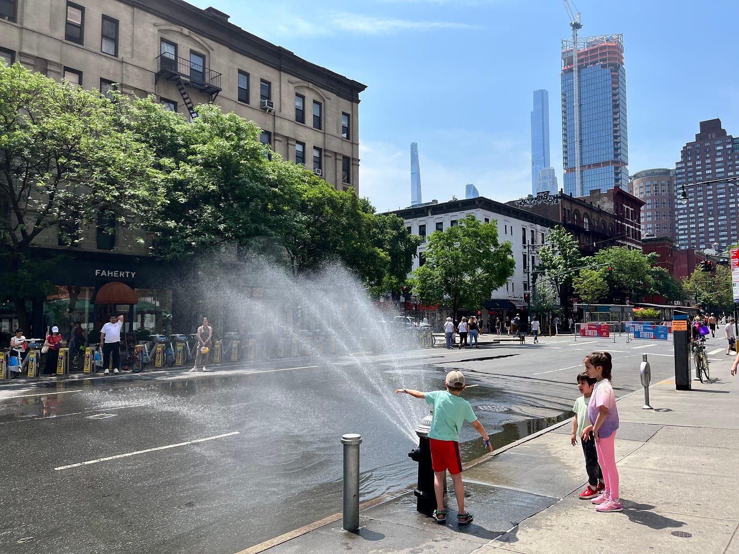 Children playing in the water sprayed by a fire hydrant in new york city with skyscrapers in background and blue sky