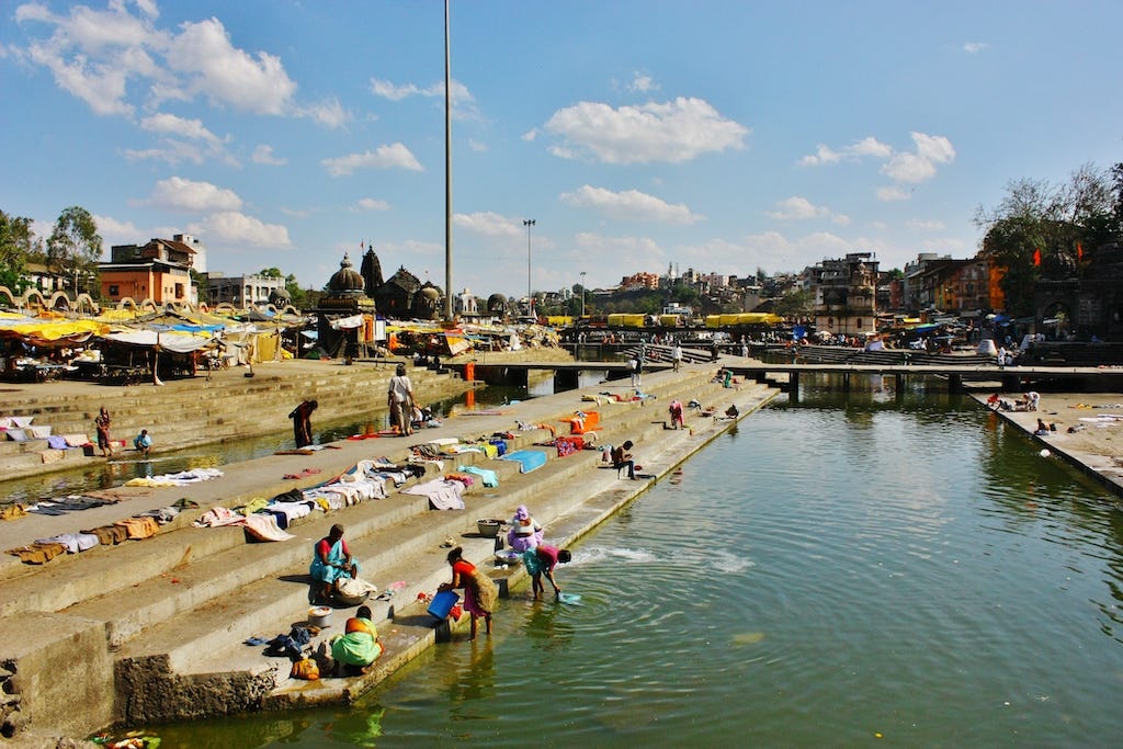 Fotografia a colori di Nashik. Si notano diverse donne che lavano i vestiti nel fiume e poi li stendono al sole ad asciugare.