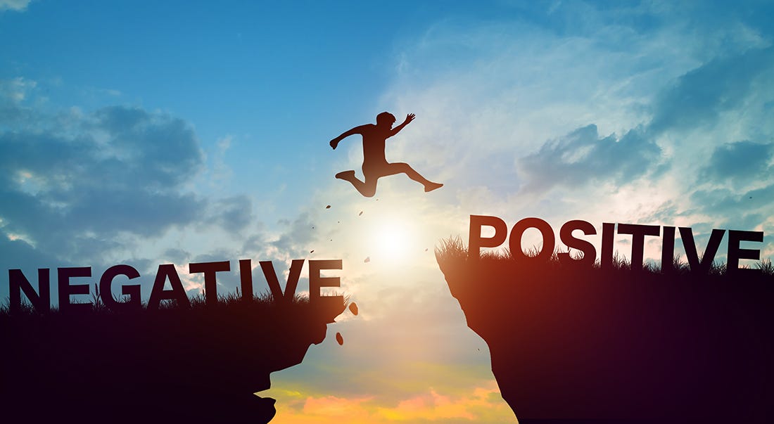 A person leaping across a chasm from a negative sign to a positive sign.