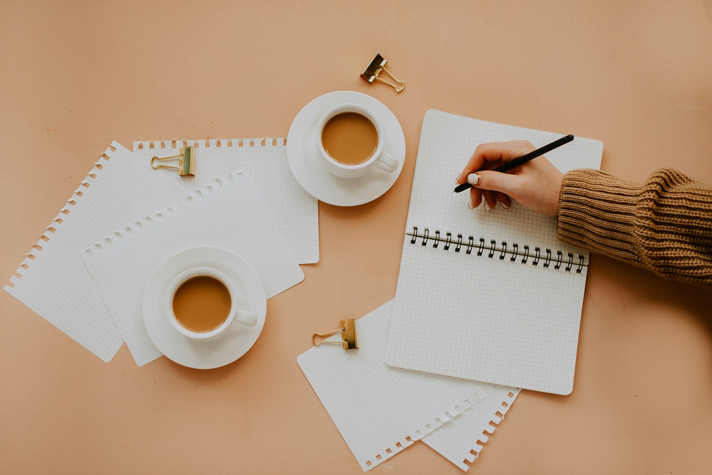 photo of flat lay of notebooks and coffee cups with a hand writing in a notebook