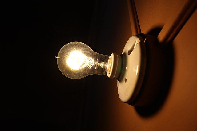 Photograph of a lightbulb, mounted on a wall in a darkened room