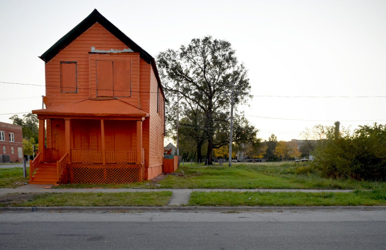 A single abandoned wooden house that is boarded up and painted dark orange in an American city.