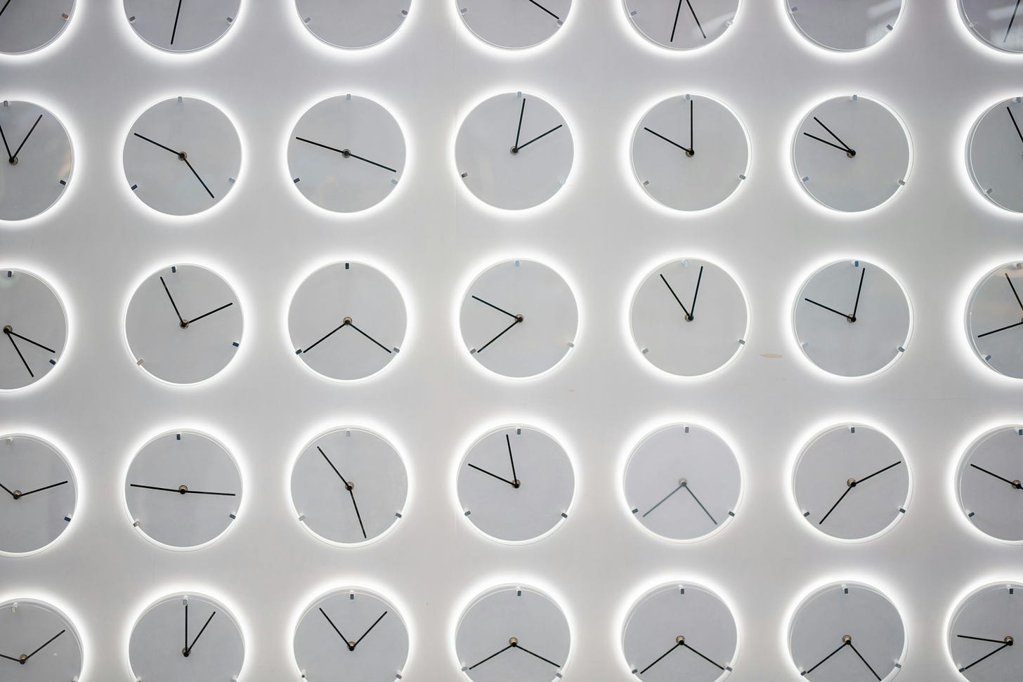 white clocks with black hands in rows and columns all showing different times