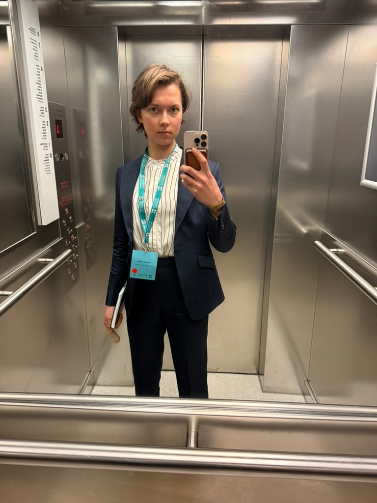 The author in a suit in an elevator. She's wearing a split.