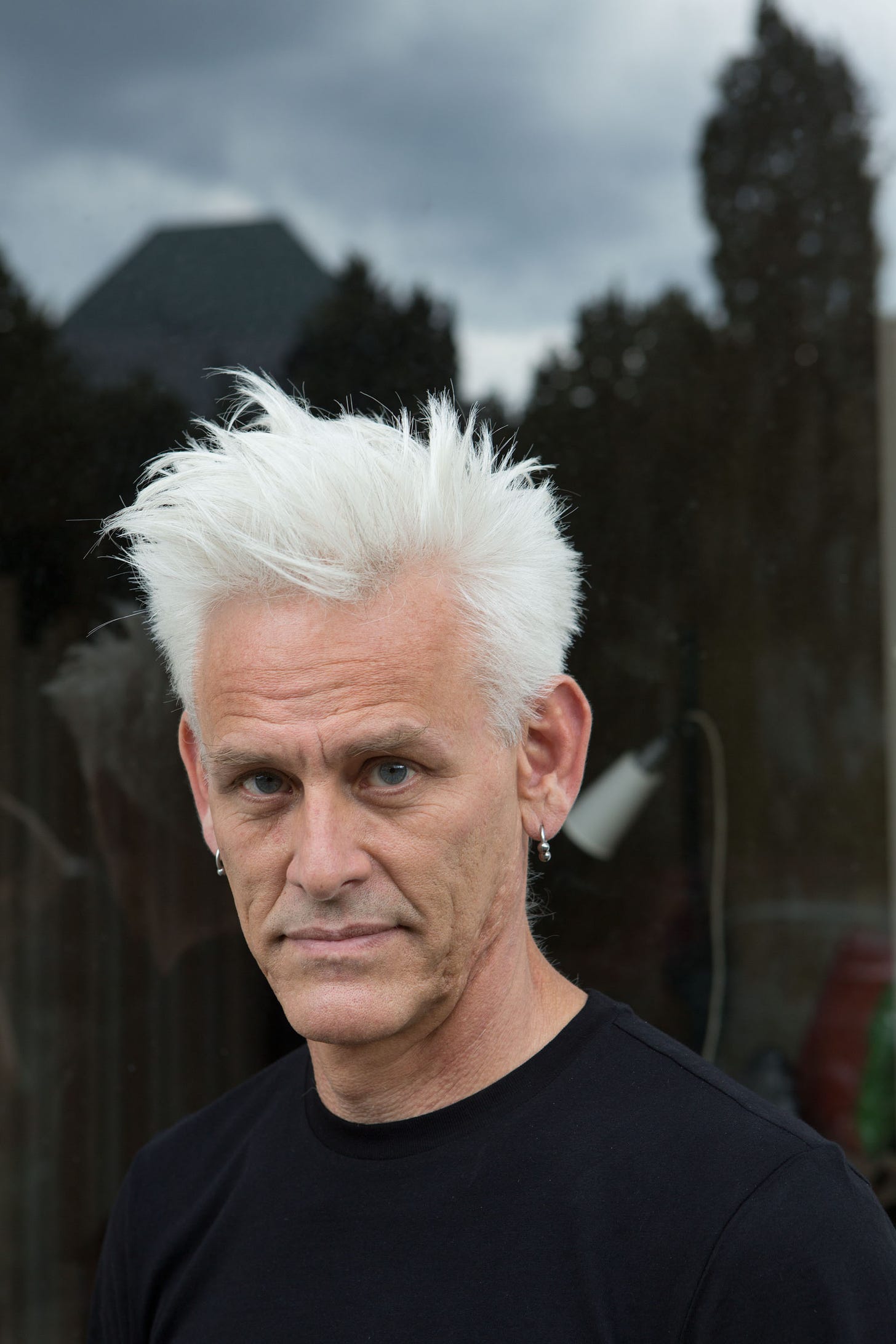 Jess Curtis wears a black tee shirt and silver earrings. He has a shock of white hair and looks into the camera. (photo: Sven Hagolani)