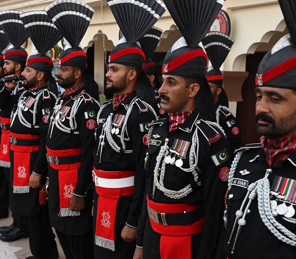 Soldiers in black and red uniforms stand at attention. 