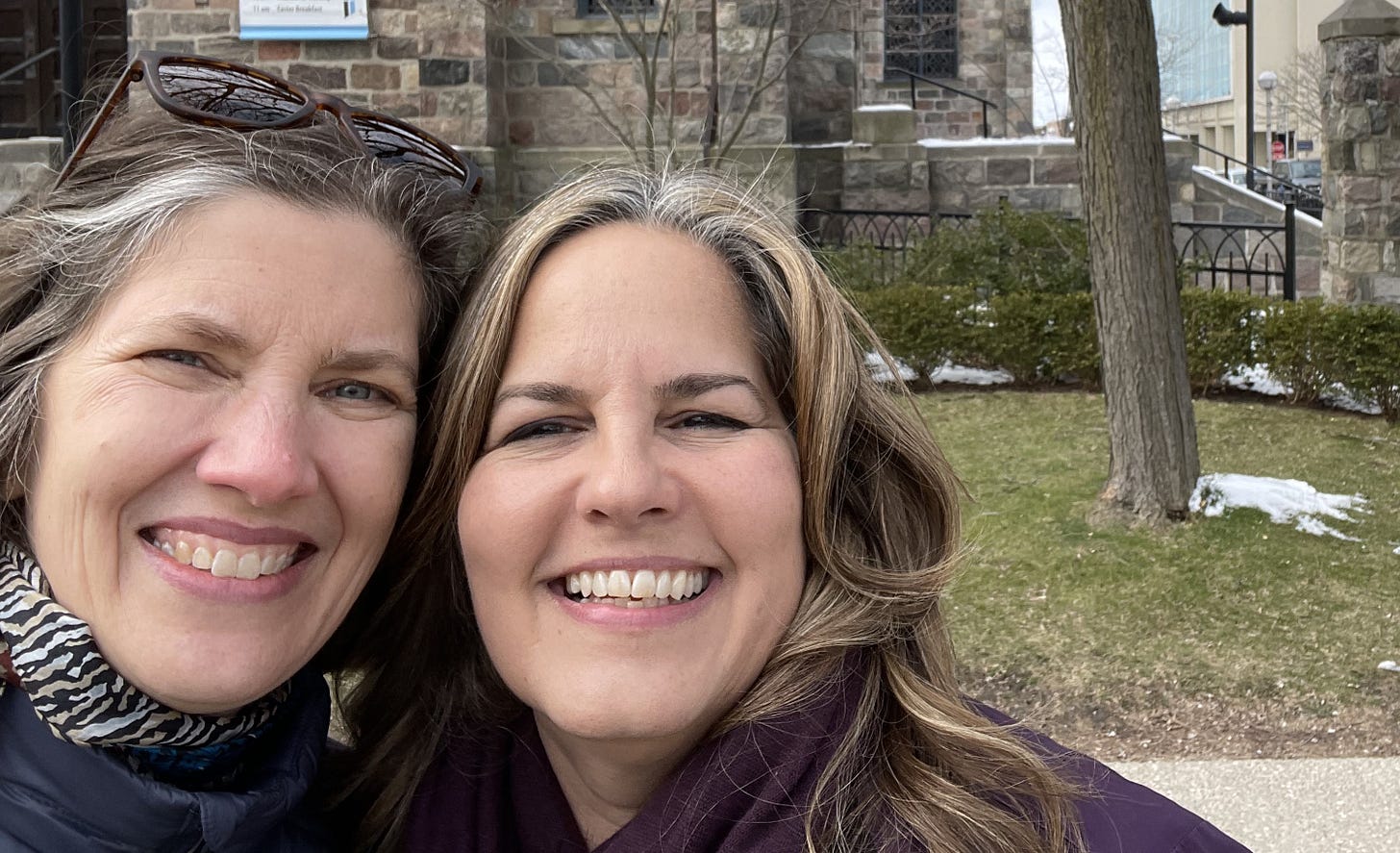 Two woman smile in front of a stone building. It's chilly, and I might have a drip coming off the end of my nose.