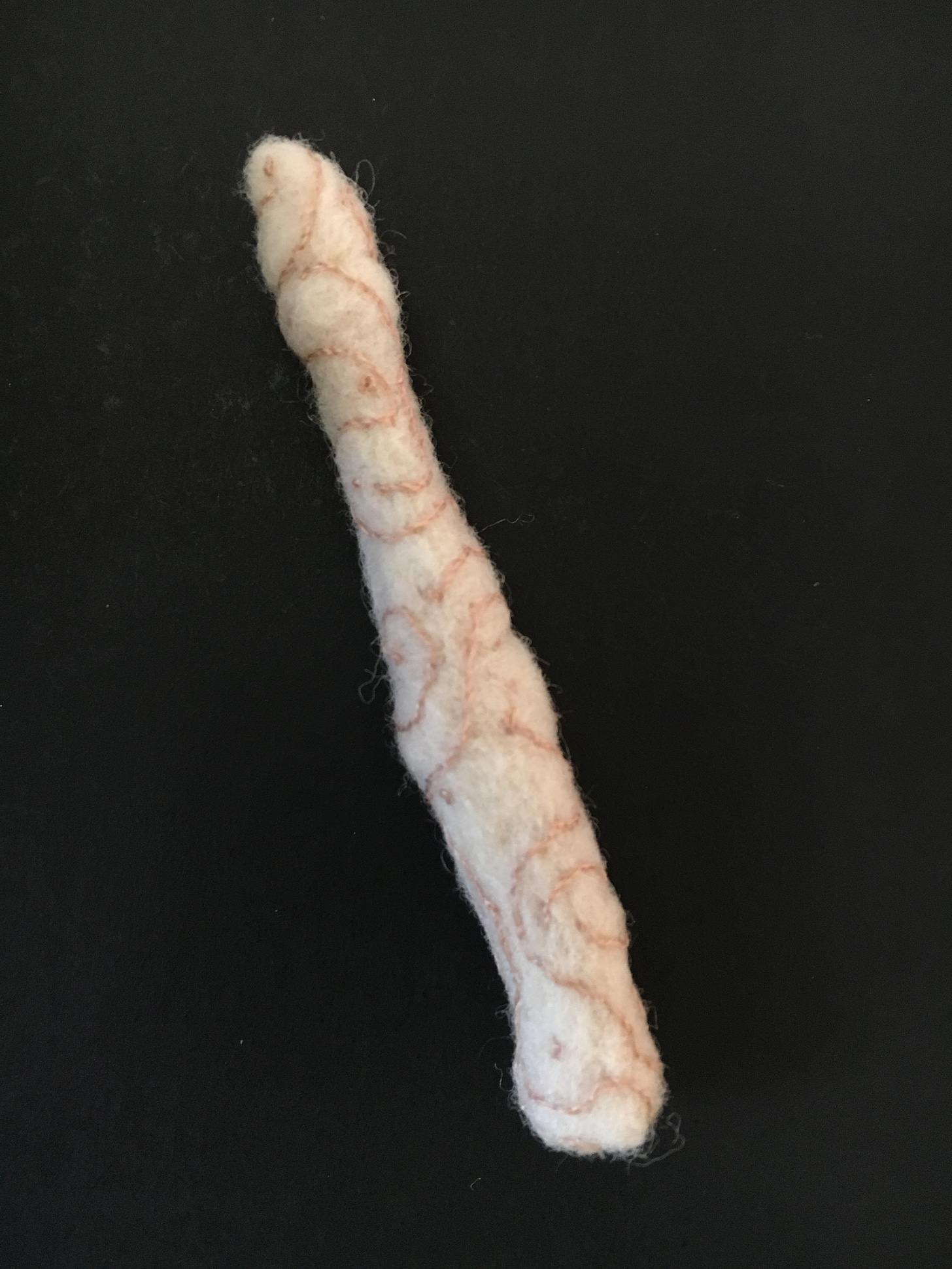 A life-sized needle felted finger bone in bone coloured wool with rose brown freehand stitching in curves and French knots.