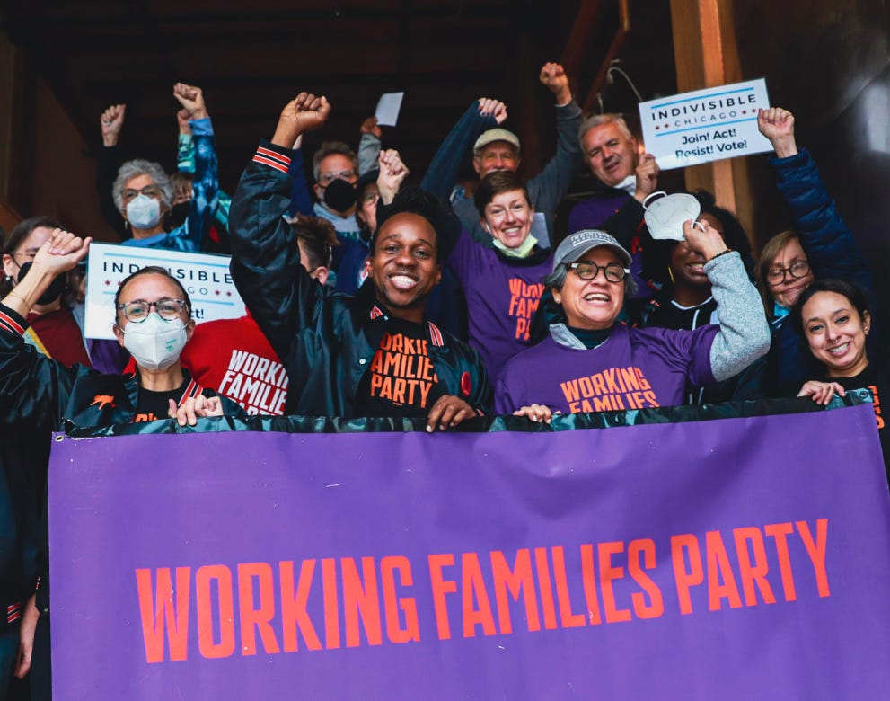 People gathered behind a banner that says "working families party", holding up their fists. Maurice, a dark skinned black man, is standing behind the sign in the middle smiling, with multiple people standing on either side of him.