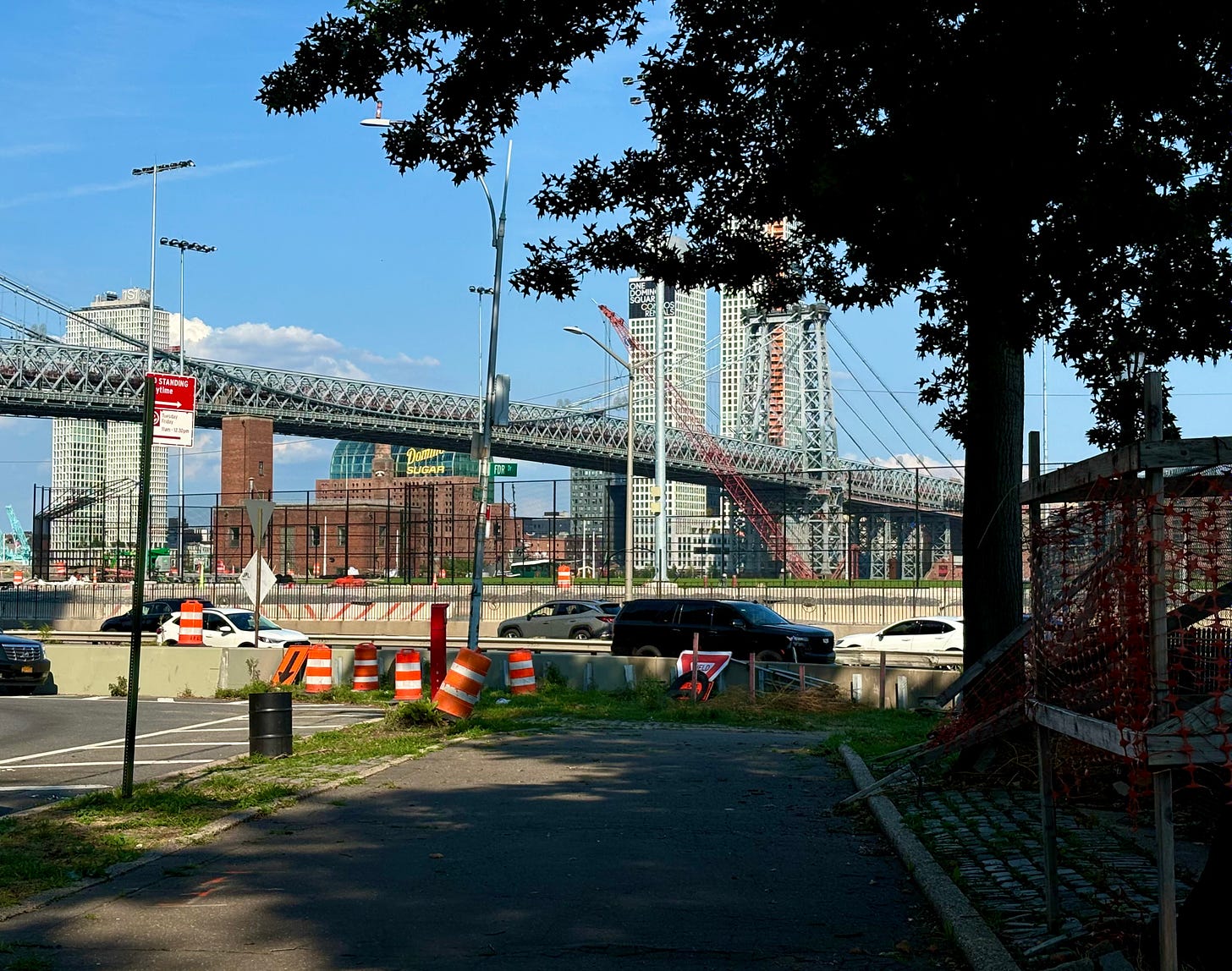 The old Domino Sugar Factory from Corlears Park. The bridge cuts across the roof and cars drive by on the FDR.