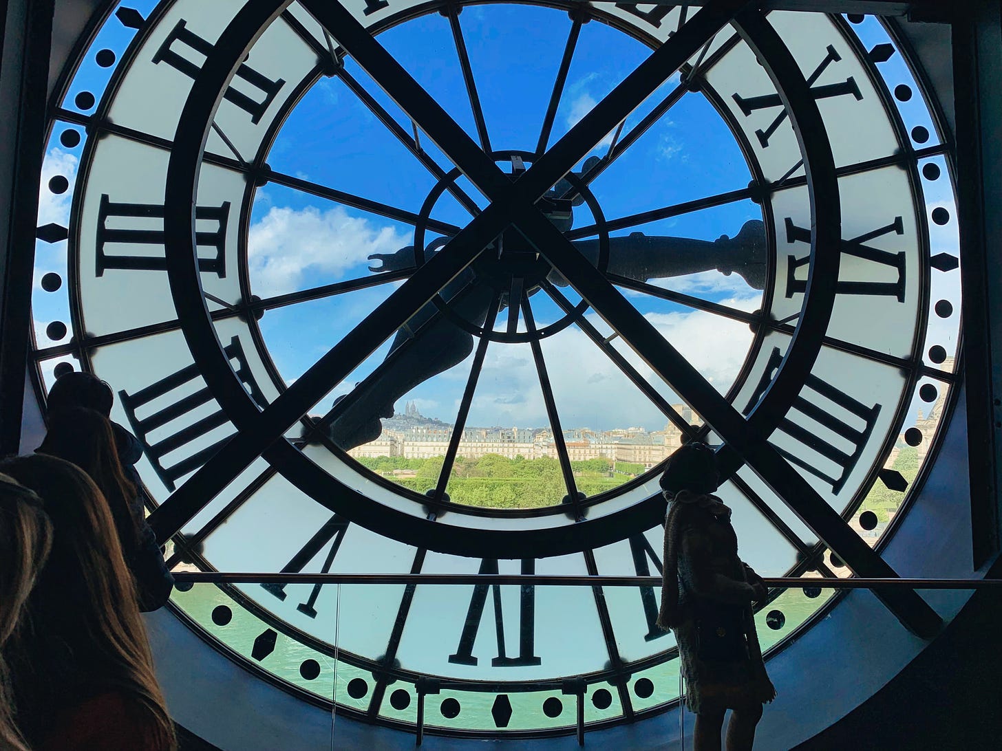 The Clock at the Muse d’Orsay with the landscape of Paris seen through the center and the silhouettes of two observers on the left and right