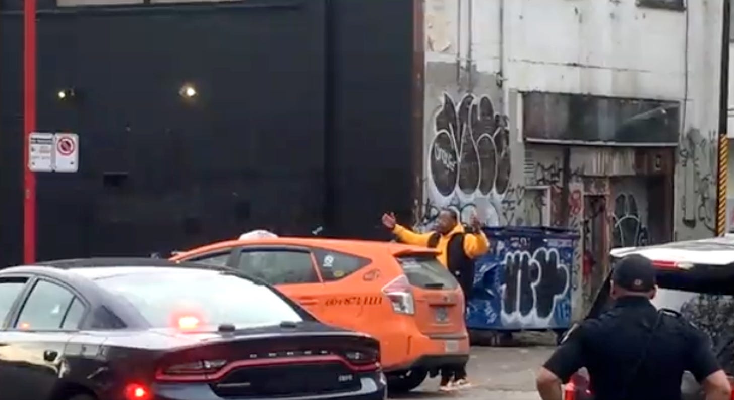 Jermaine Johnson is seen facing an orange taxi with his hands in the air in the Downtown Eastside.