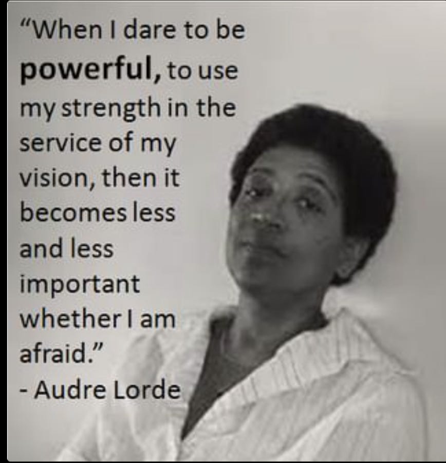 The image is of Audre Lorde. She is a Brown skinned Black woman with a short afro. Audre is smiling. The image includes a quote by Audre Lorde about being powerful and unafraid. It is in black and white and includes text elements.