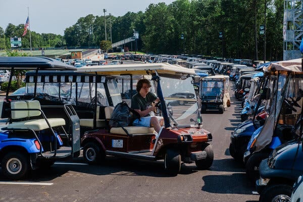 A student in a golf cart pulls out of a spot in a crowded lot filled with carts. 