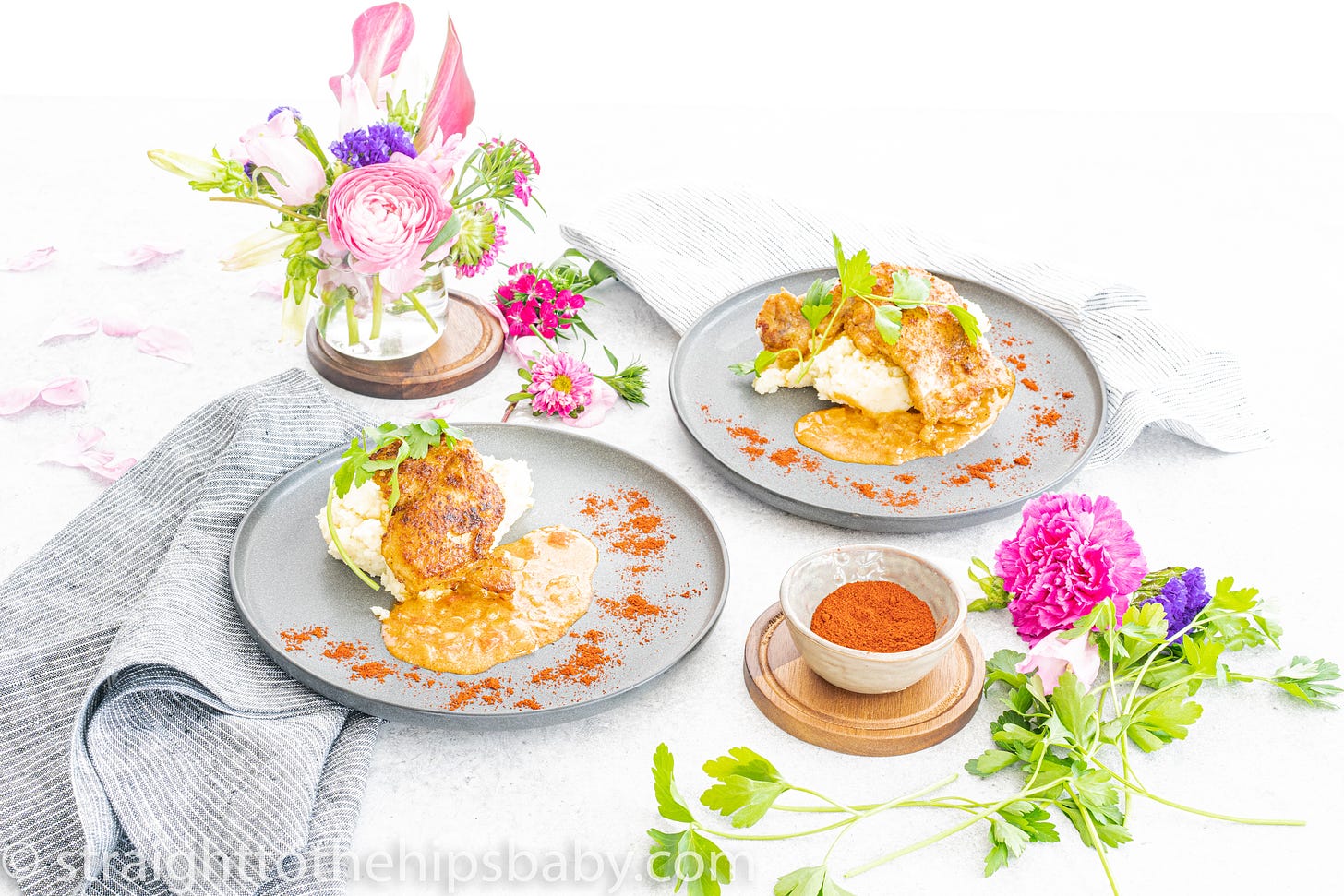 Food on light grey plates with flowers displayed in a glass on the side of the table. 