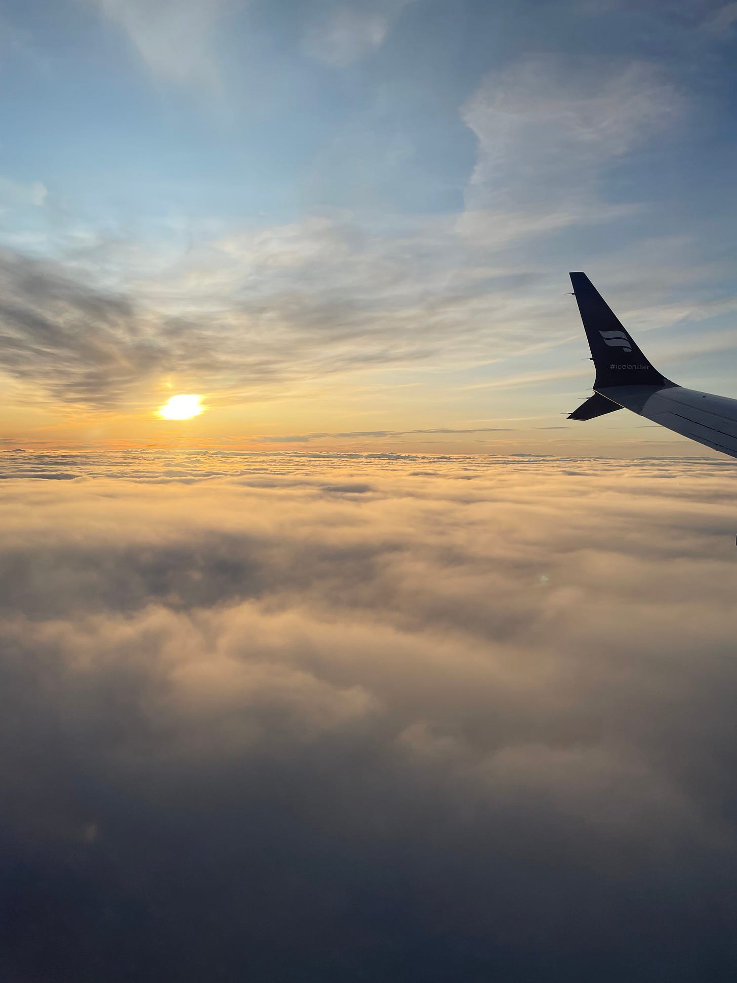 The view out a plane window, all clouds with the sun visible past the wing