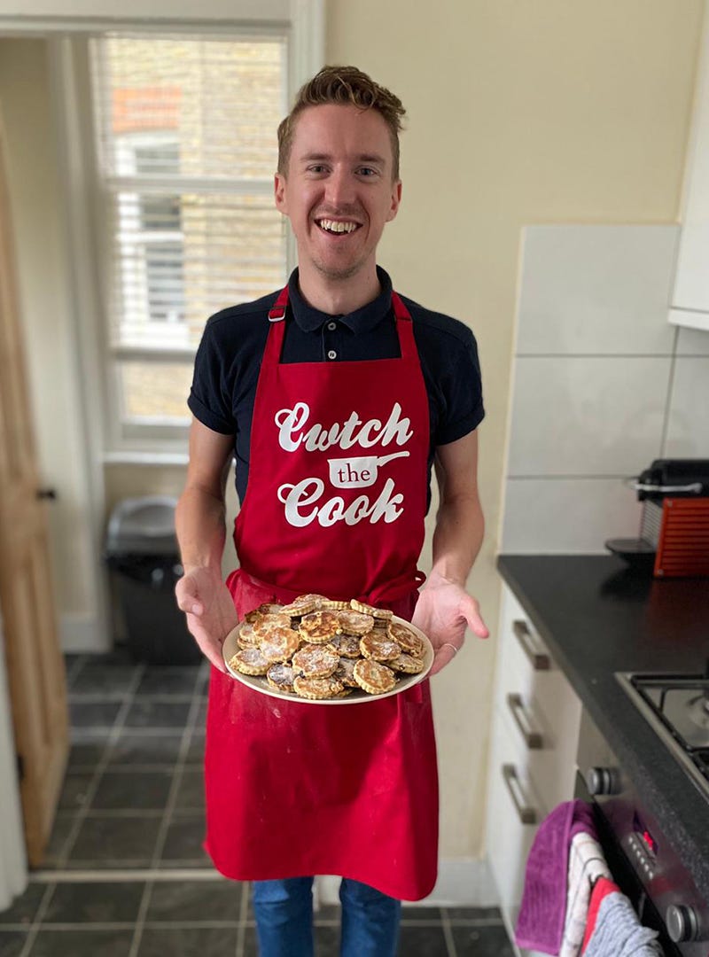 Ross Clarke wearing red Cwtch the Cook apron holding a plate of Welsh cakes