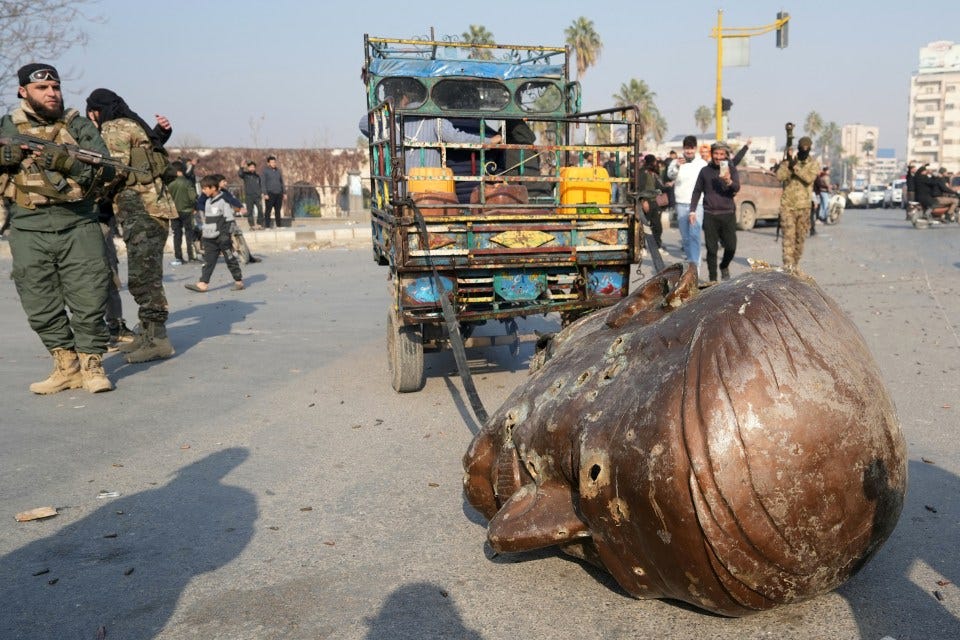 A truck pulls the head of the toppled statue of Assad's father Hafez al-Assad in Hama