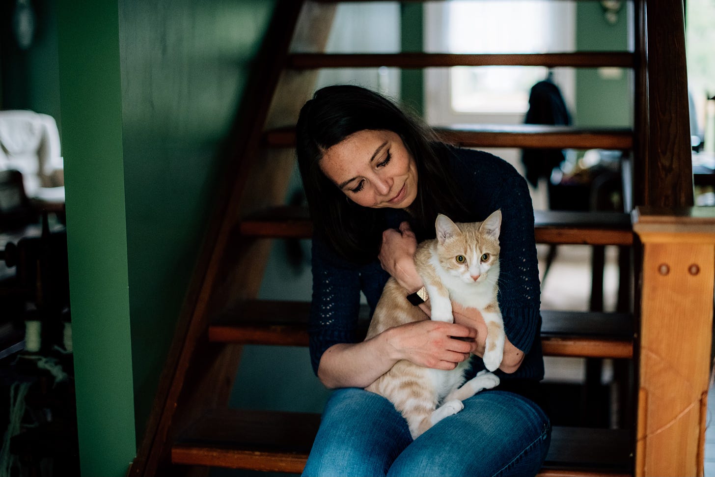 Woman sits on stairs cuddling an orange tabby cat
