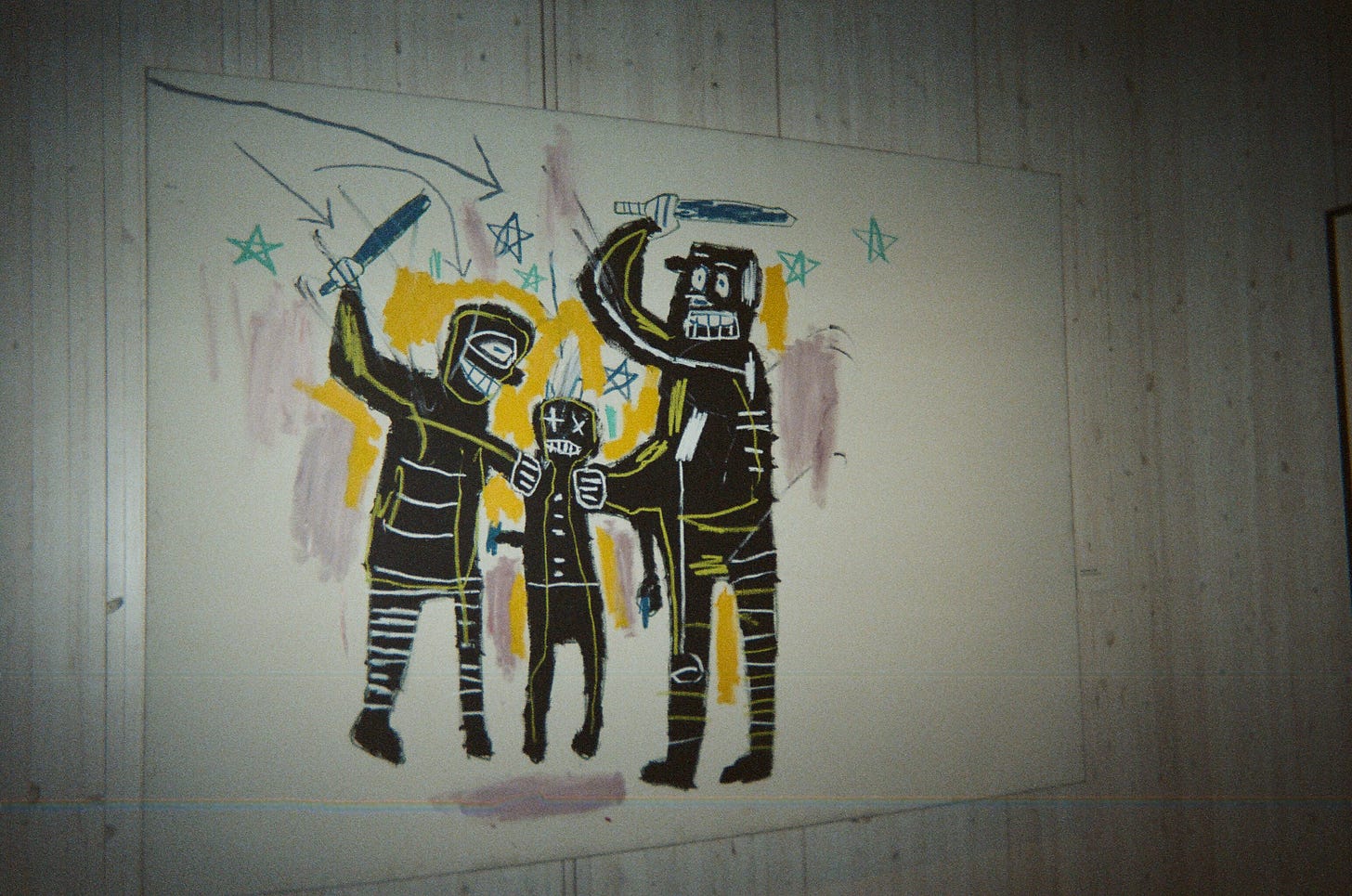 a picture of a portrait done by Basquiat: two police officers take batons to a Black boy holding a gun. The way he’s drawn the figures mimics a silhouete, with yellow and mauve colored in a round them. Stars radiate from the center of the piece, reminiscent of the way stars catapult from cartoon character’s heads when they get knocked around.