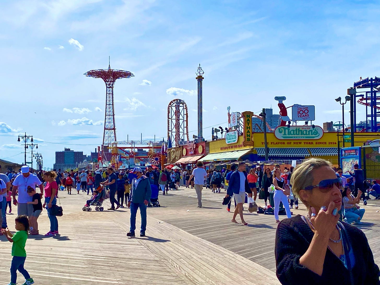 A summer's afternoon on Ocean Avenue. Crowd's dressed brightly and casually walk between the amusement park and Nathan's.